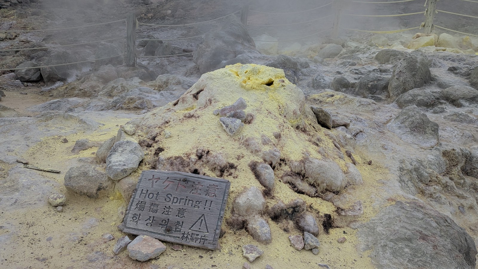 アトサヌプリの噴気孔に積もった黄色い硫黄の結晶とHot Springの標識