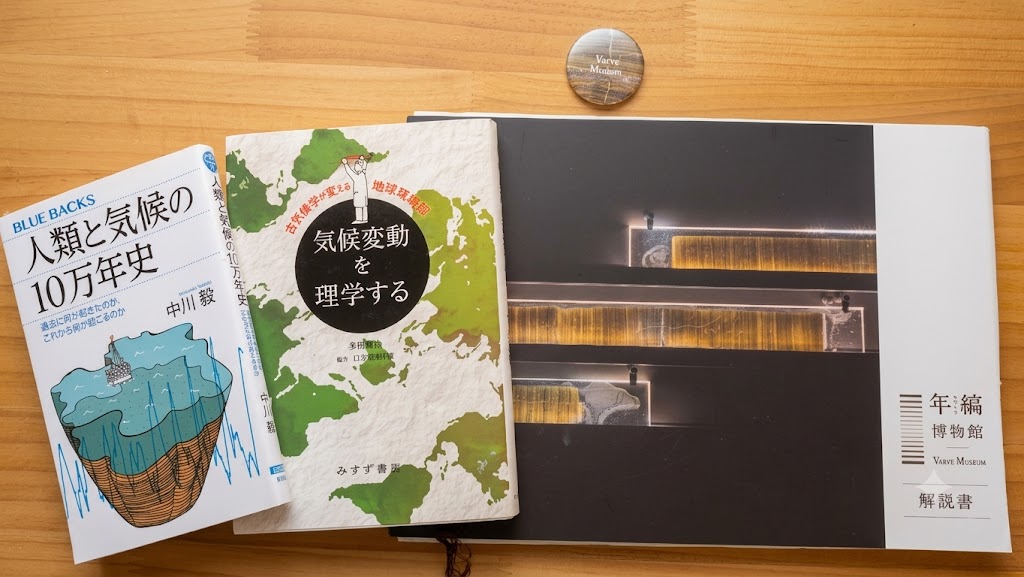 年縞博物館の公式解説書と金色のミュージアムバッジ、中川毅の著書2冊が机に並ぶ