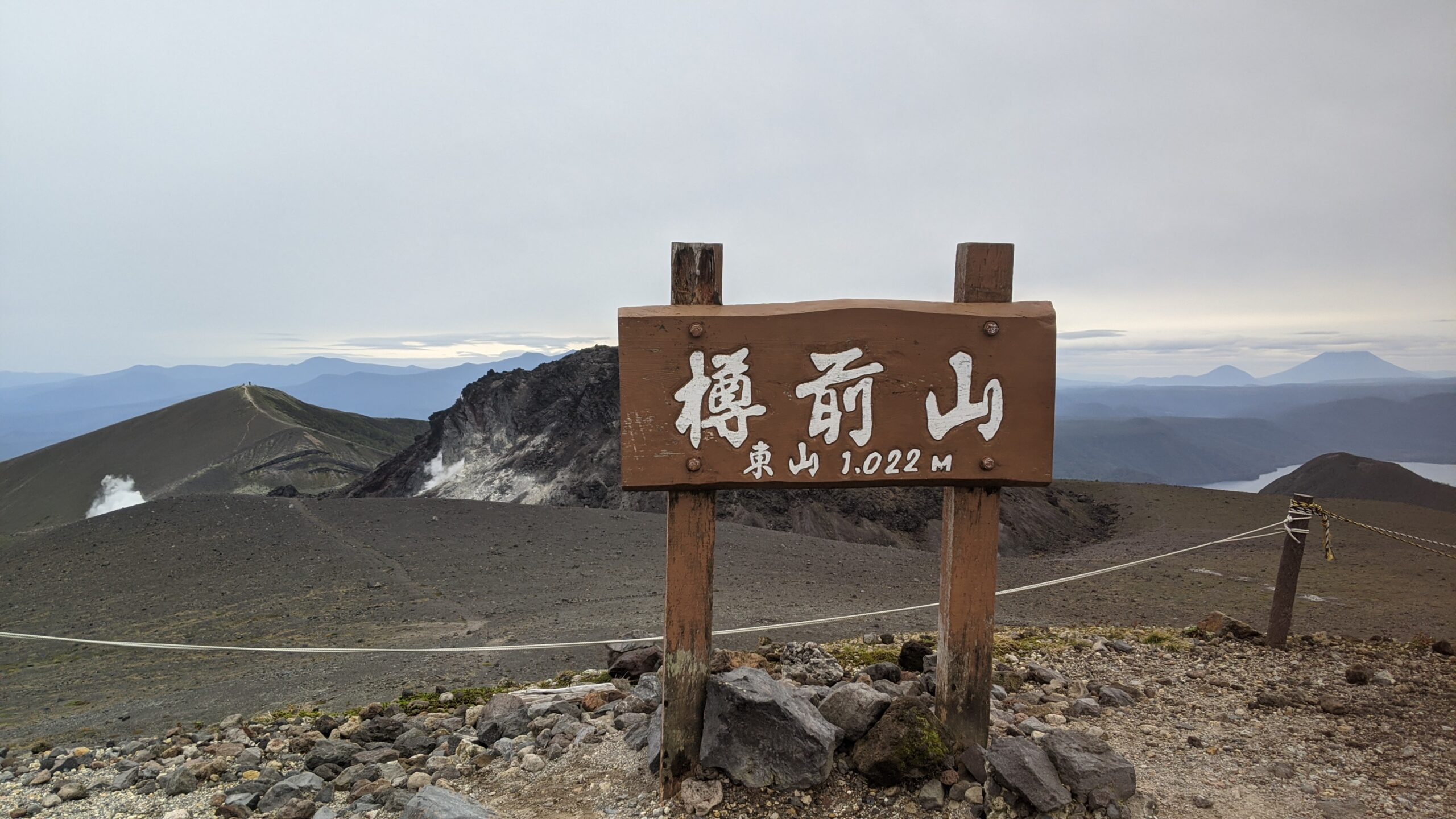 樽前山東山山頂の標識と火口原。遠景に支笏湖と羊蹄山