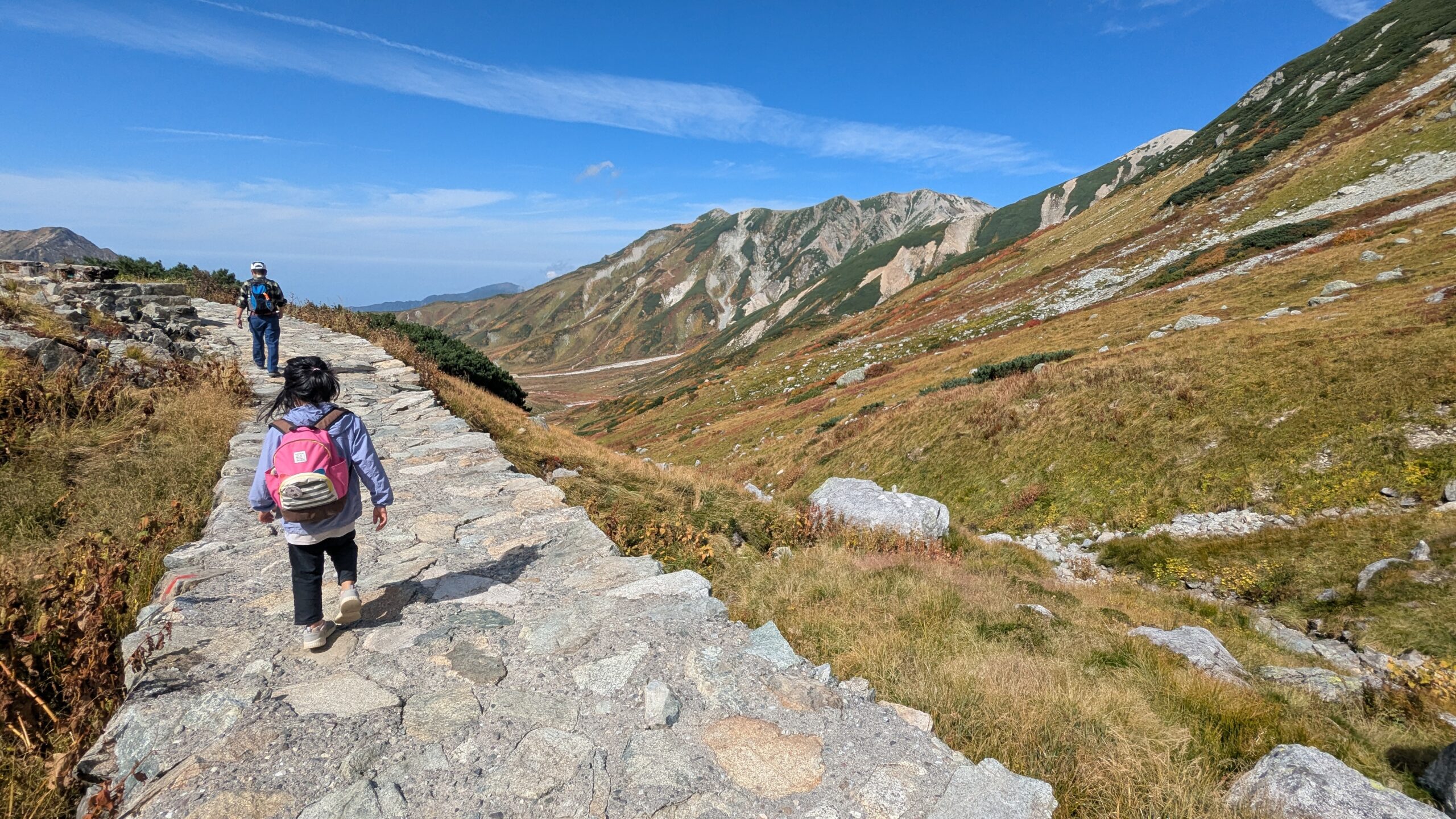 一ノ越へ続く石畳の道を歩く子どもの後ろ姿。周囲は紅葉の始まった立山の山肌