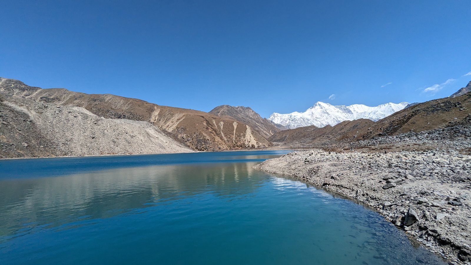 ゴーキョ湖と乾いた土色の山肌、奥に雪をかぶった8000m級の峰